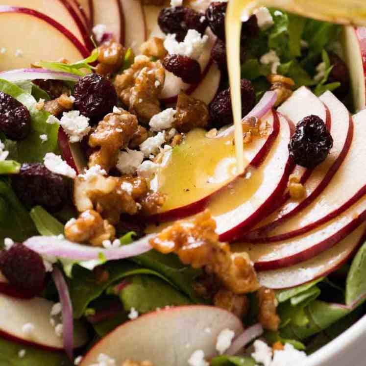 Vinaigrette being poured over Apple Salad with Candied Walnuts and Cranberries