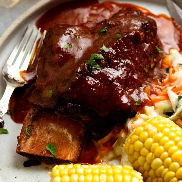 Beef Ribs in barbecue sauce on a plate with coleslaw and corn