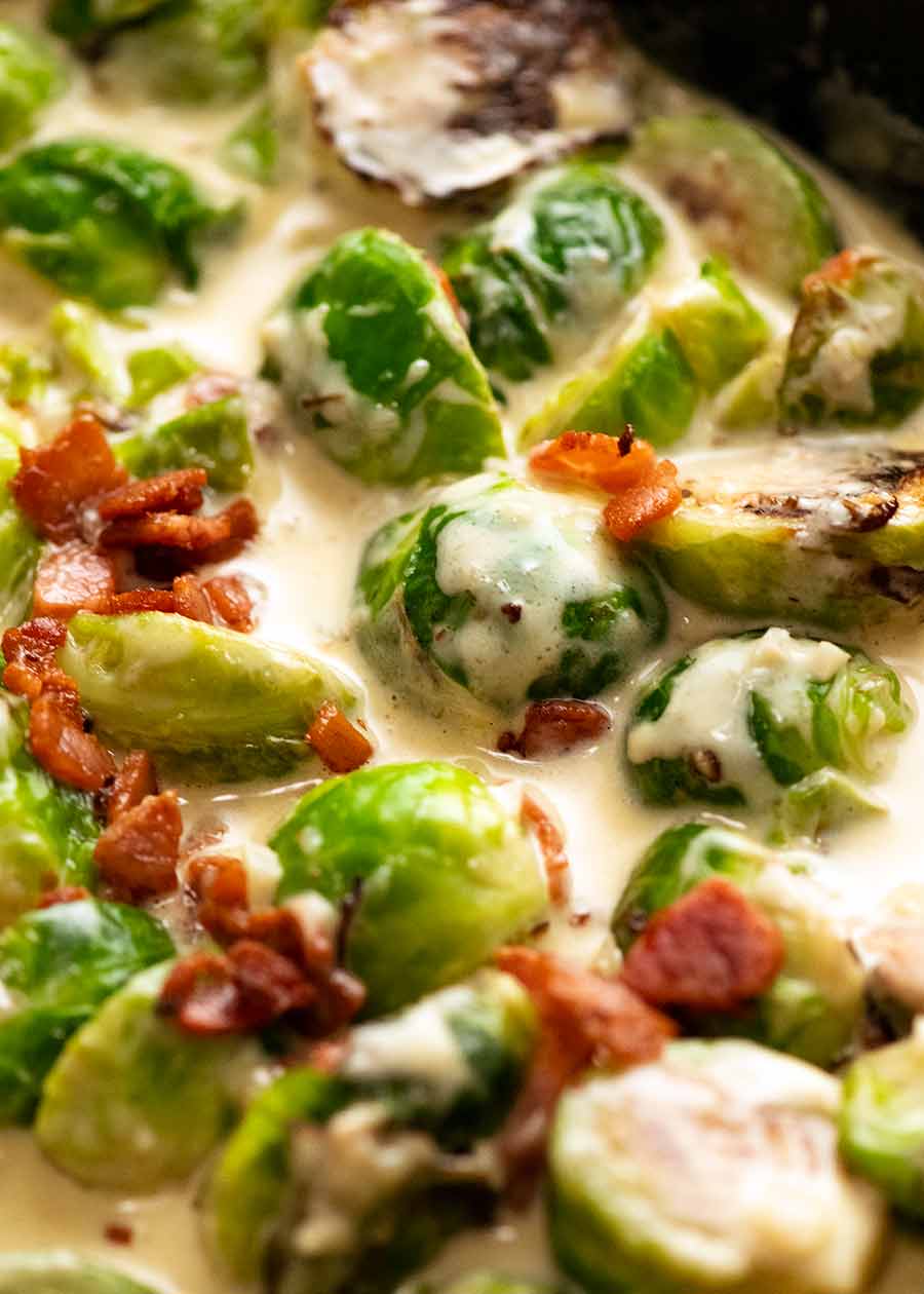 Close up of Brussels Sprouts in a creamy sauce with bacon in a skillet