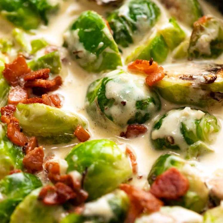 Close up of Brussels Sprouts in a creamy sauce with bacon in a skillet