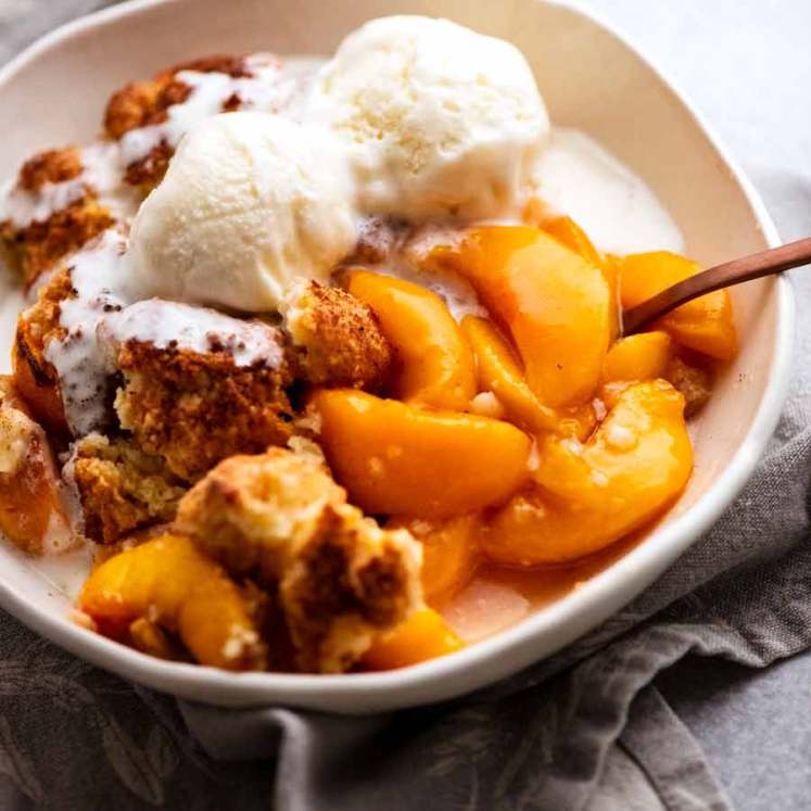 Peach Cobbler in a bowl topped with vanilla ice cream