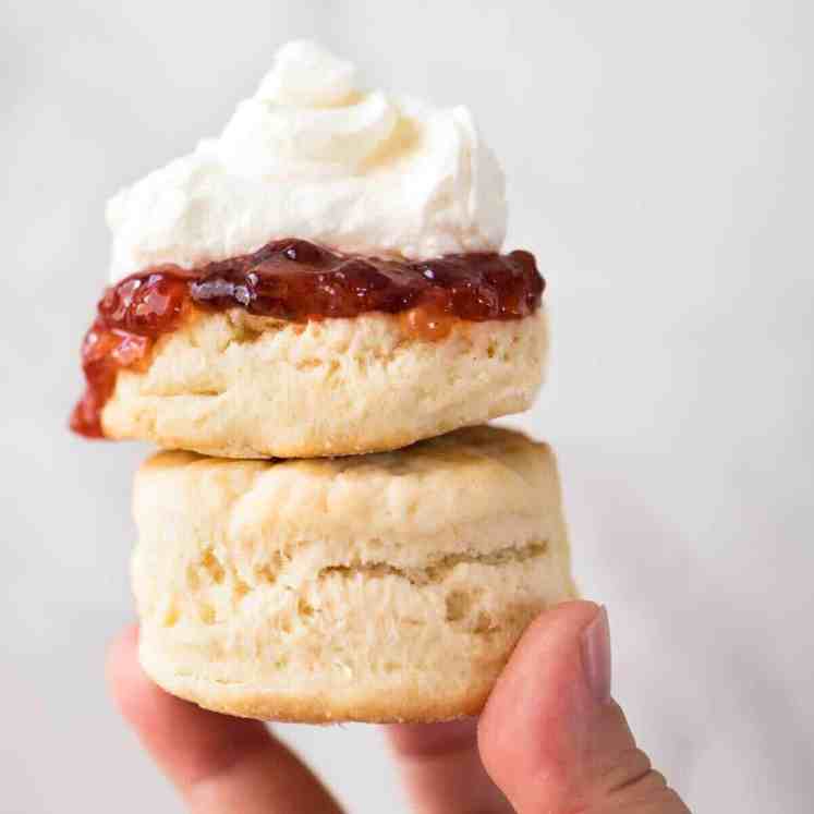 Close up of a plain scone with jam and cream being held up high, stacked on top of another scone.
