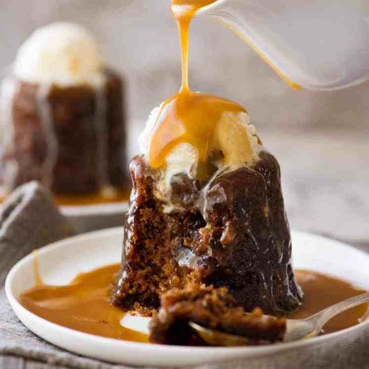 Butterscotch Sauce being poured over Sticky Toffee Pudding on a white plate, ready to be eaten