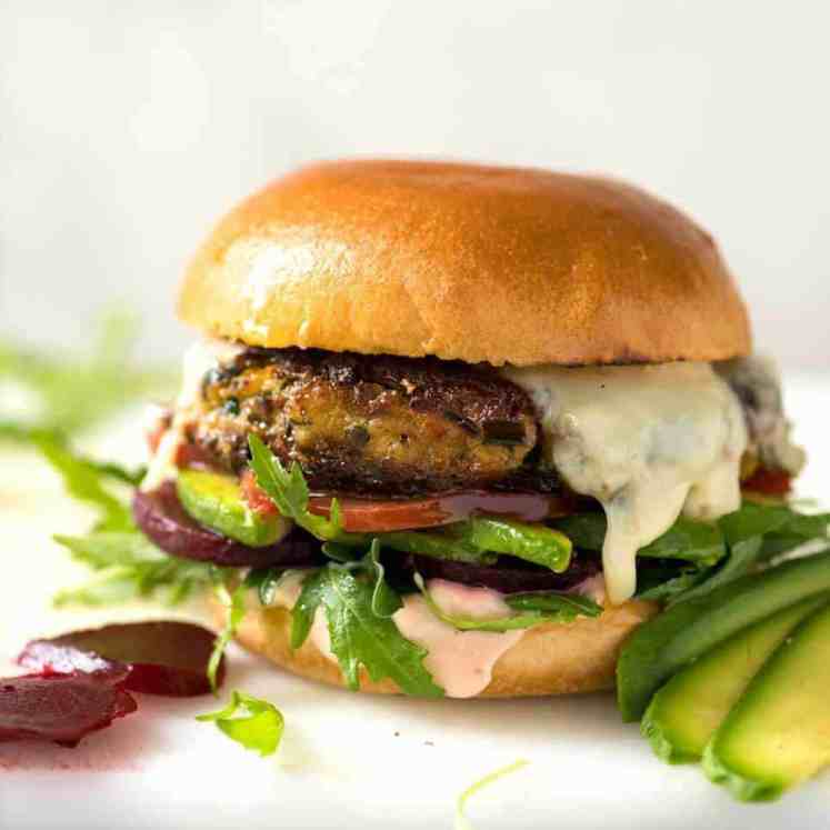 A veggie burger with melted cheese, avocado, beetroot, tomato and lettuce on a soft golden bun.