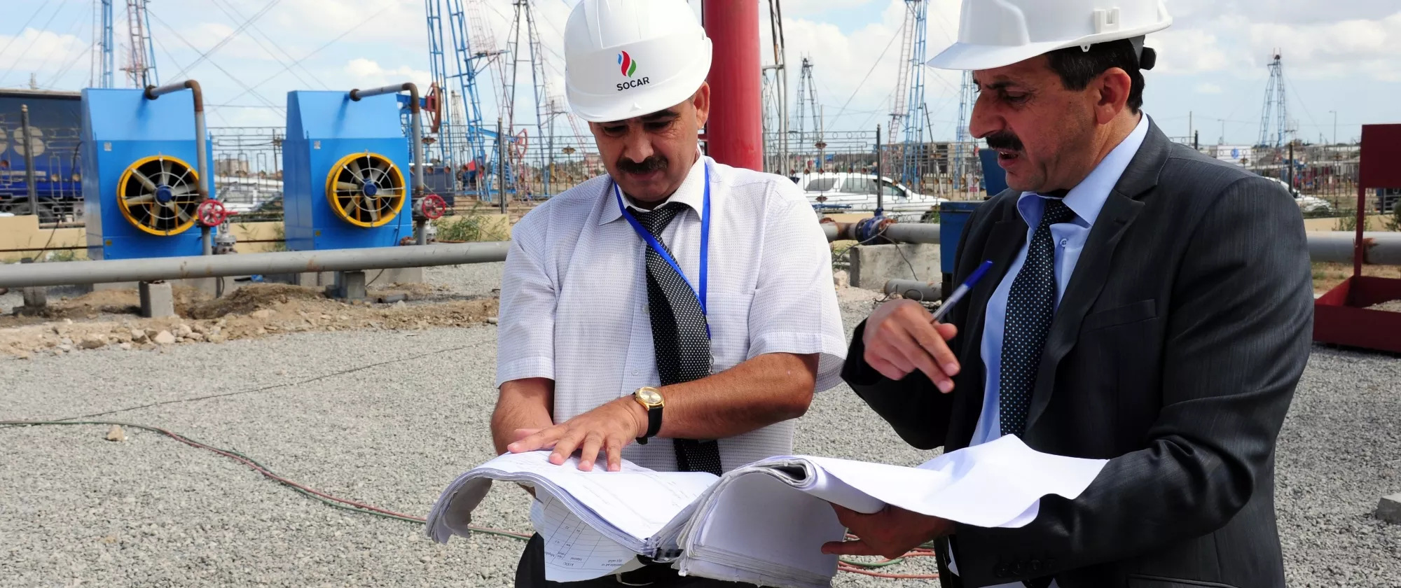 Two men in suits and protective helmets look over documents at a working site in Azerbaijan. 