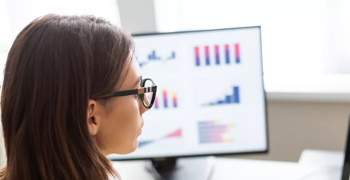 A woman sitting looking at a data dashboard graphs on two screen