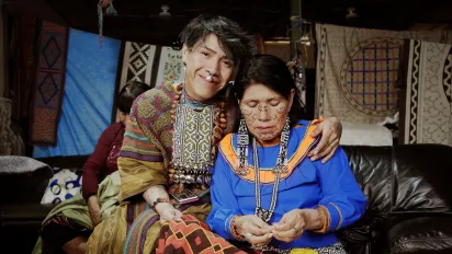 Young man with peircing with arm around woman sewing, both in traditional dress