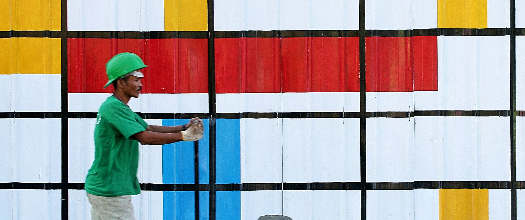 Man pushing a cart with paint buckets in front of a colourful wall.