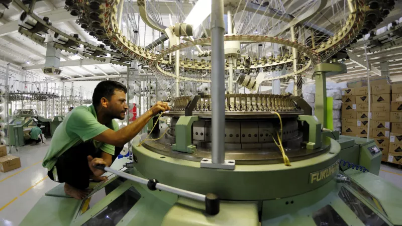 This is a photograph of a specialized garment worker at work on a complex piece of machinery in a clothing factory in Bangladesh 